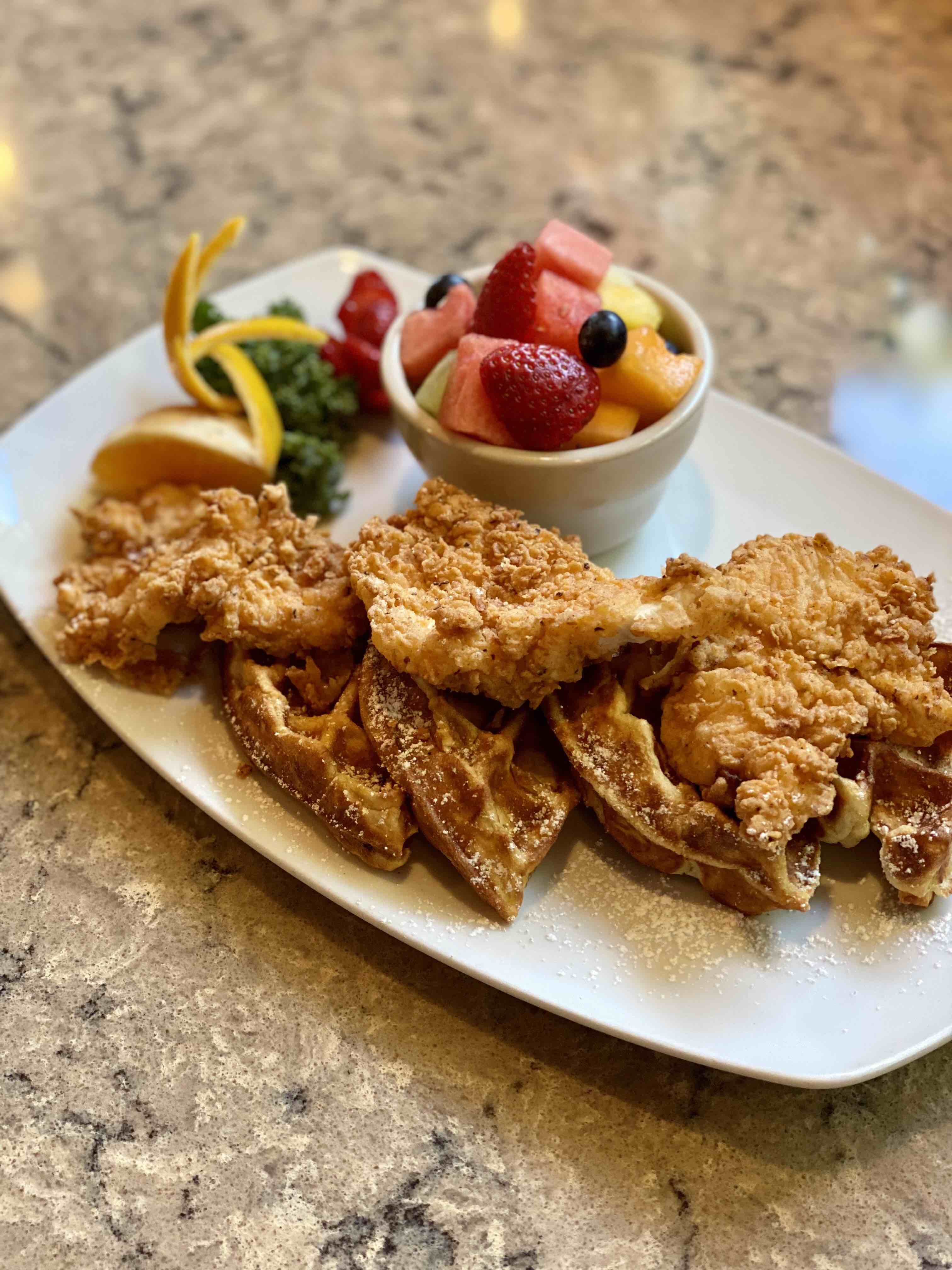 chicken and waffles with a cup of fruit