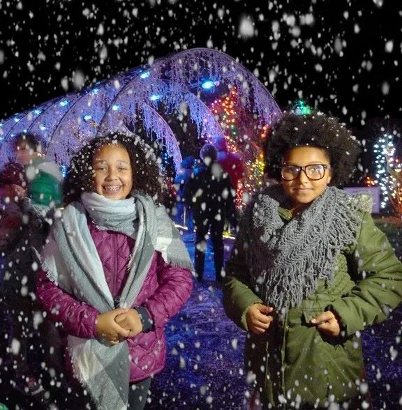 two girls stand under fake snow machine