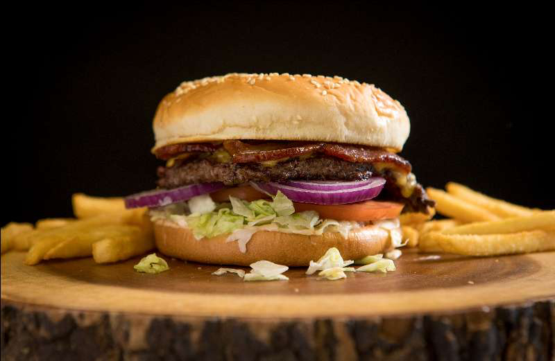 Burger on a wooden stump with onions and bacon