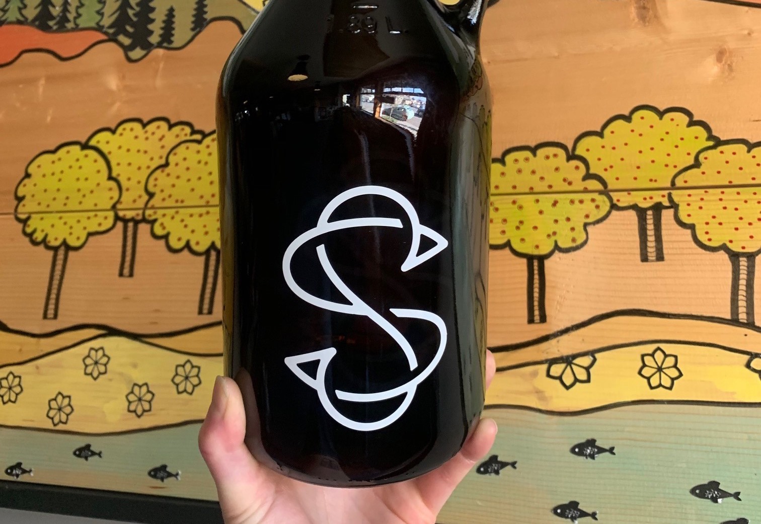 close up of hand holding growler with S logo on outside