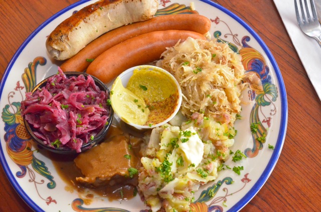 Plate with sausages, sauerkraut, potatoes, and gravy.