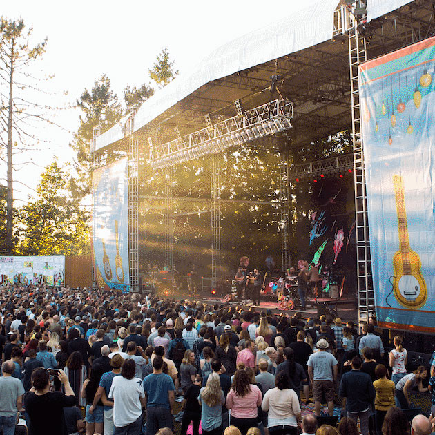 Large group of people watch concert outside as sun sets