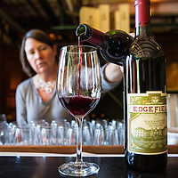 woman pours bottle of red wine into glass next to bottle of Edgefield wine