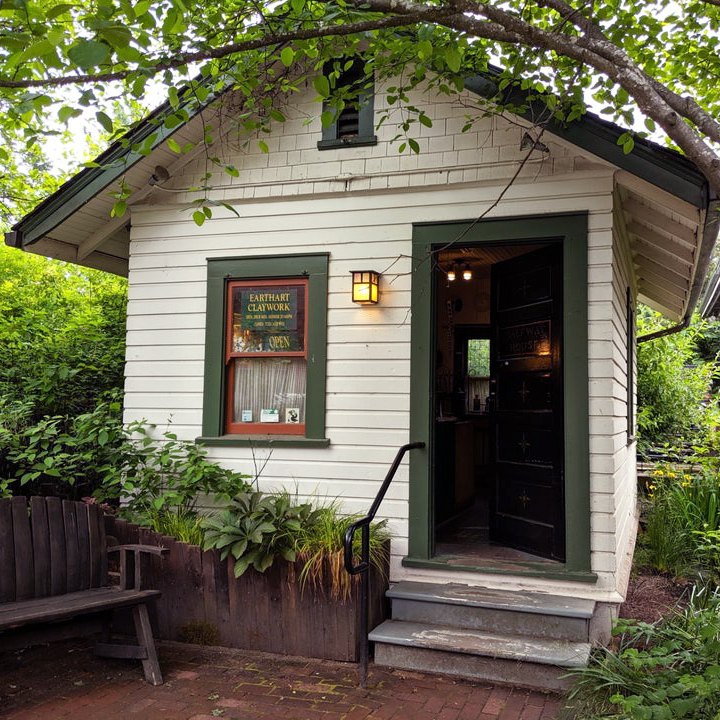 Small old building with 2 steps nestled in the trees houses Earthart Clayworks