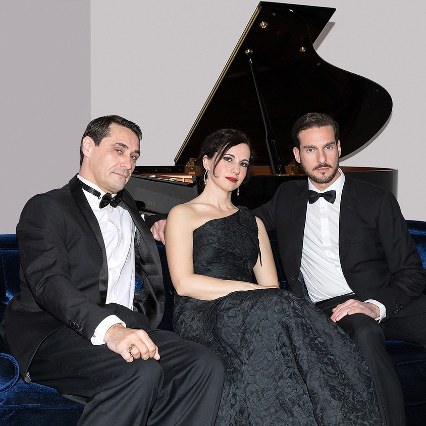 two men and one women in black and white sitting on coach infront of piano