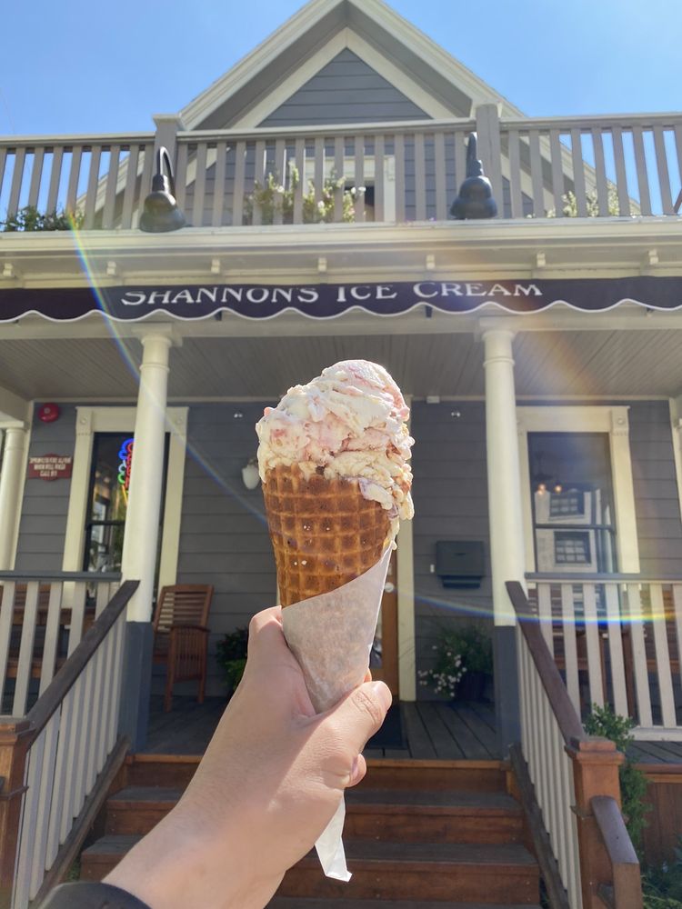 hand holding ice cream cone infront of ice cream shop