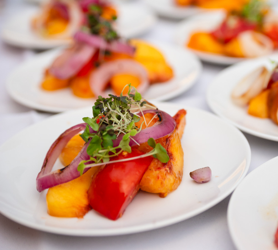 picture of multiple plates with one in the foreground, grilled peaches, onions and micro greens