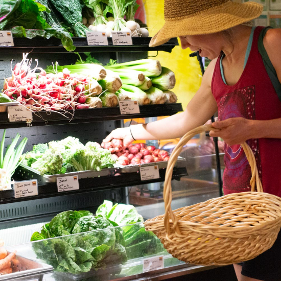 woman in straw hat and basket shown grabbing potatoes from a refrigerated produce shelf