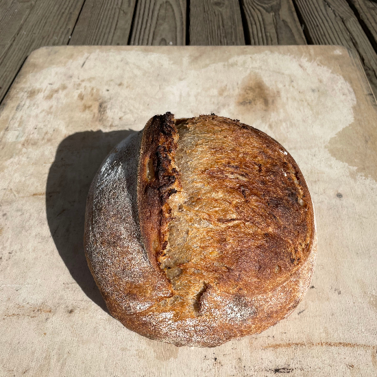 Loaf of bread on wooden cutting board on picnic table outdoors