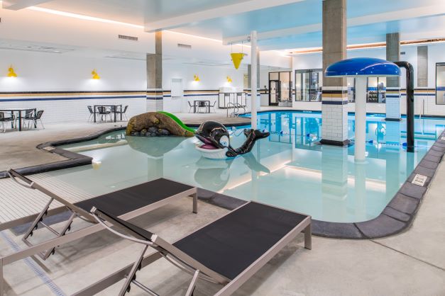 indoor hotel pool and play area surrounded by tables, chairs and chaise lounges
