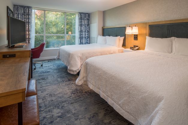 hotel guest room with two beds, desk and view of trees at the window