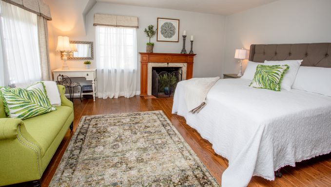 guest room with large bed, couch, fireplace and light coming in two windows