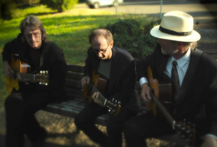Three musicians sit on a bench playing guitars
