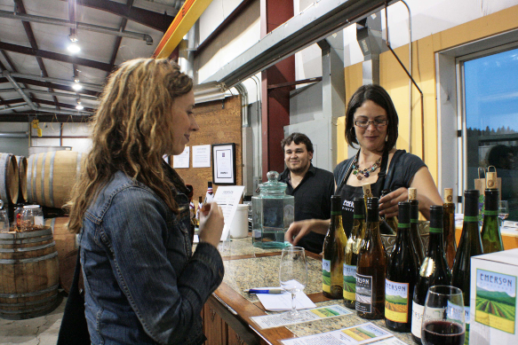 A women standing behind a counter offering different samples of wine for guests.