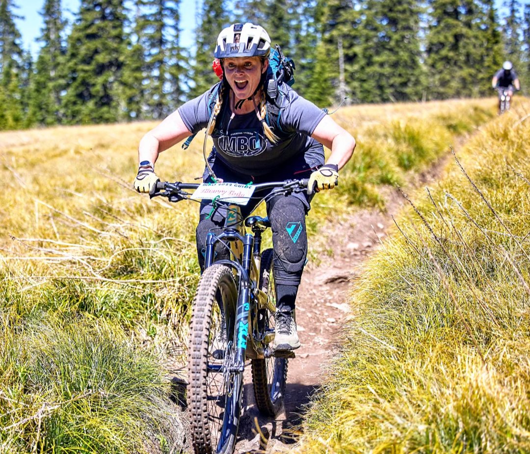 A woman mountain biking a trail in the forest on a sunny day.