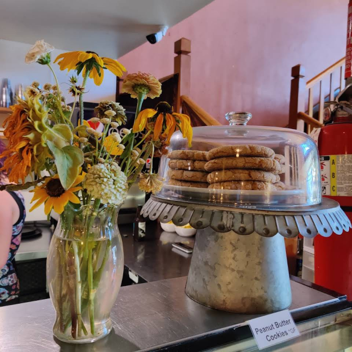 A vase of flowers standing next to a display of peanut butter cookies.