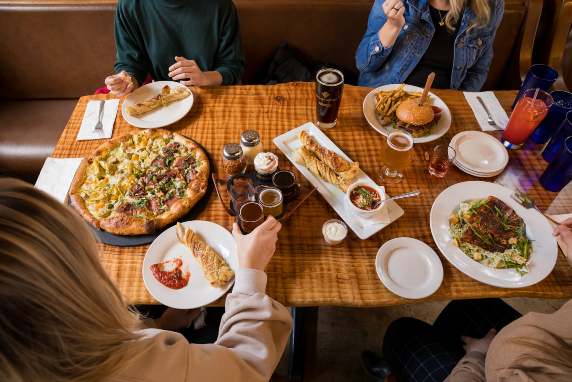 Four people sitting at a table enjoying beer and food such as pizza.