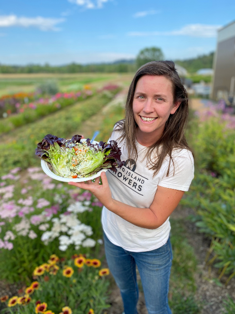 A woman holding a salad in a field of flowers.