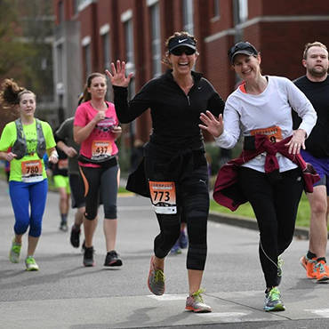 Four women and a man running during a half marathon.