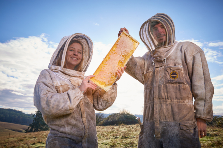 Two people posing with a beehive.