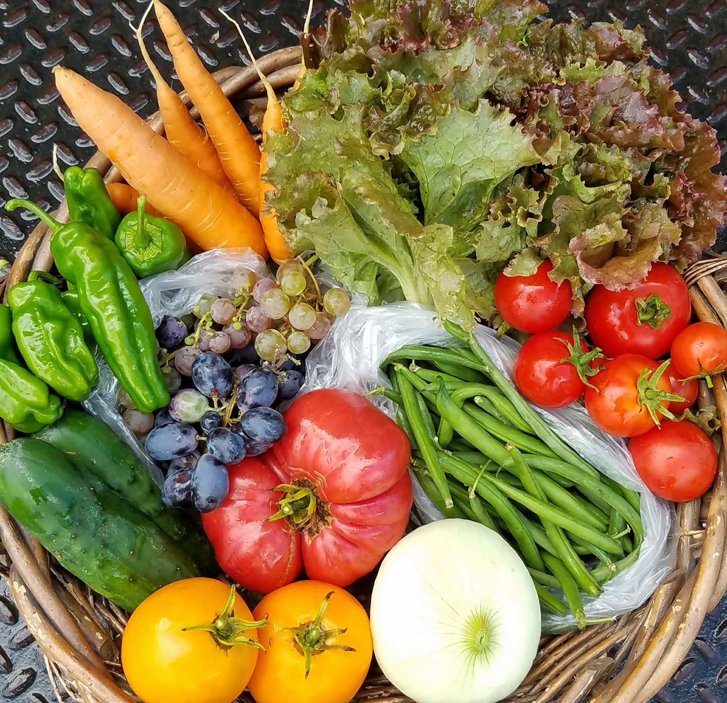 A basket full of peppers, tomatoes, grapes, and other veggies.