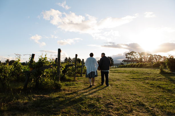 Two people walking through vineyards with the sun shinning.