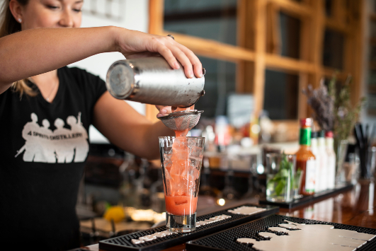 A bartender pouring a cocktail into a glass with ice.