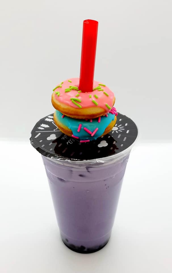 A purple boba tea with mini donuts on top of it.