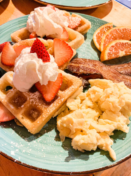 A plate of waffles, scrambled eggs, bacon, and fruit at MaMere's Guest House.