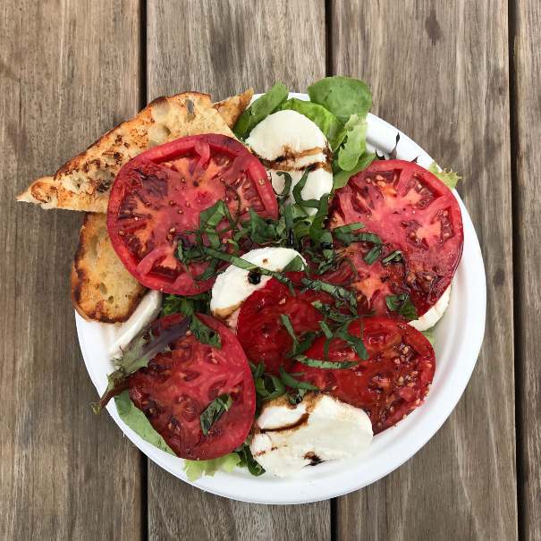 A fresh made salad with tomatoes, basil, and mozzarella served with bread.