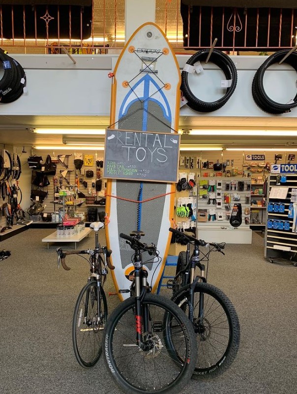 retail bike shop with display for rentals with three mountain bikes and a surf board on display