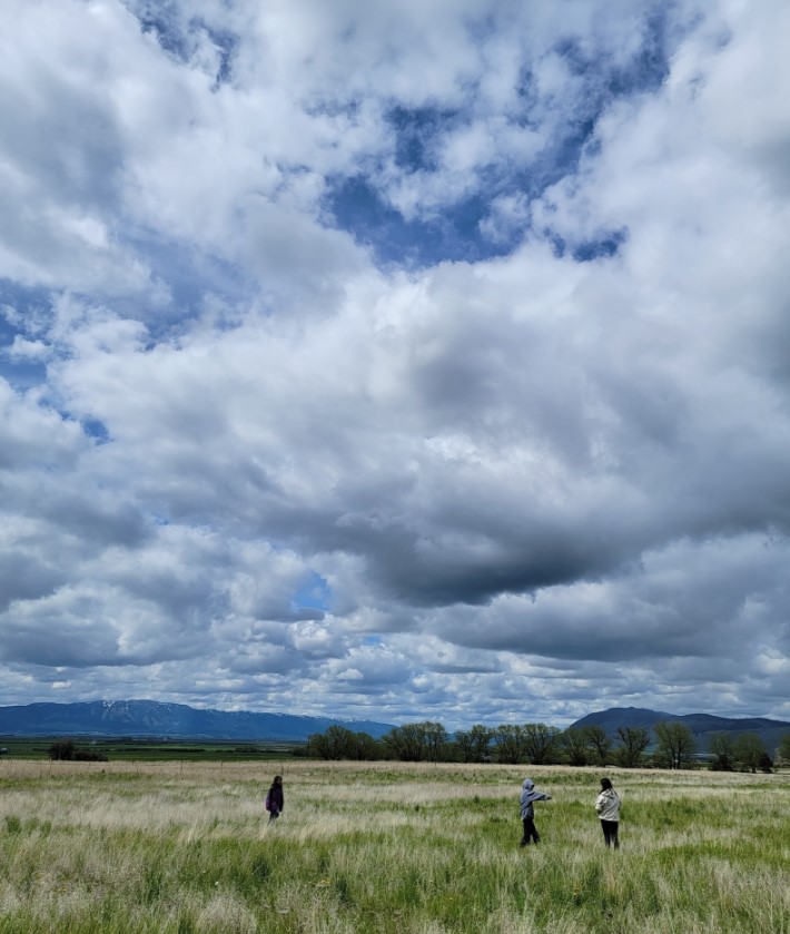 three people standing in meadow under cloudy sky