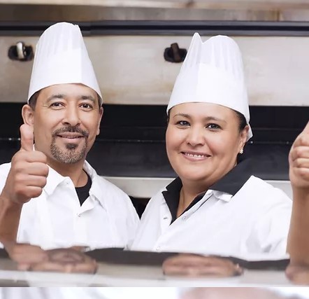 two chefs with hats smile at camera in restaurant kitchen