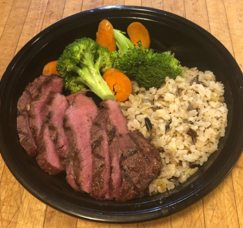 close up of entree with slices of steak cooked rare, rice, broccoli and carrots