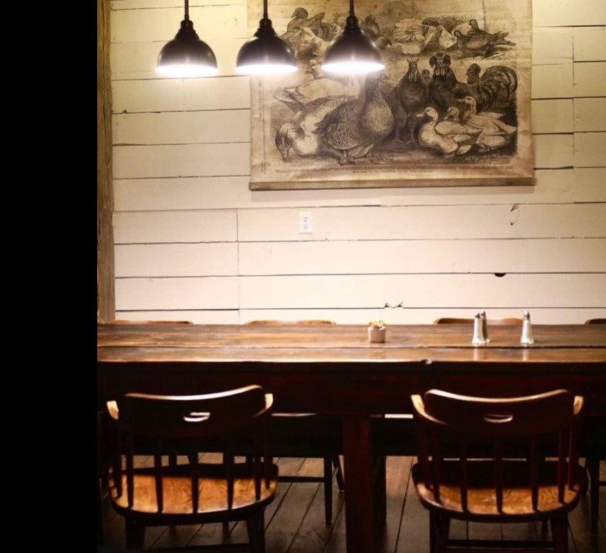 rustic wooden banquet table and chairs with overhead pendant lights and artwork at restaurant