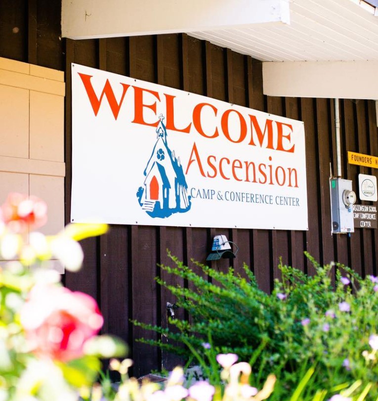 sign with text for Welcome Ascension Camp & Conference Center on outside of building with vertical wood panelling