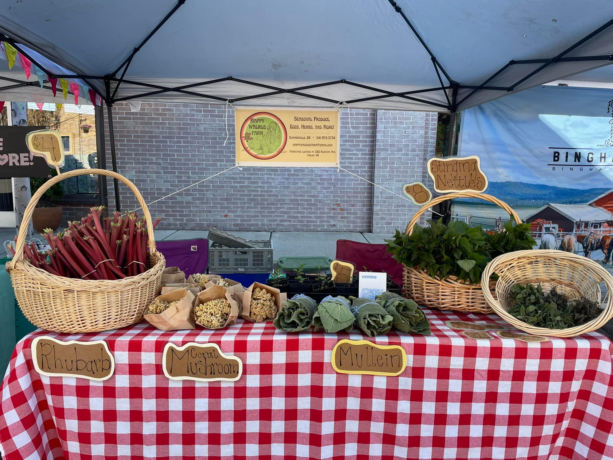 Farmers market vendor booth with baskets of produce and herbs on display