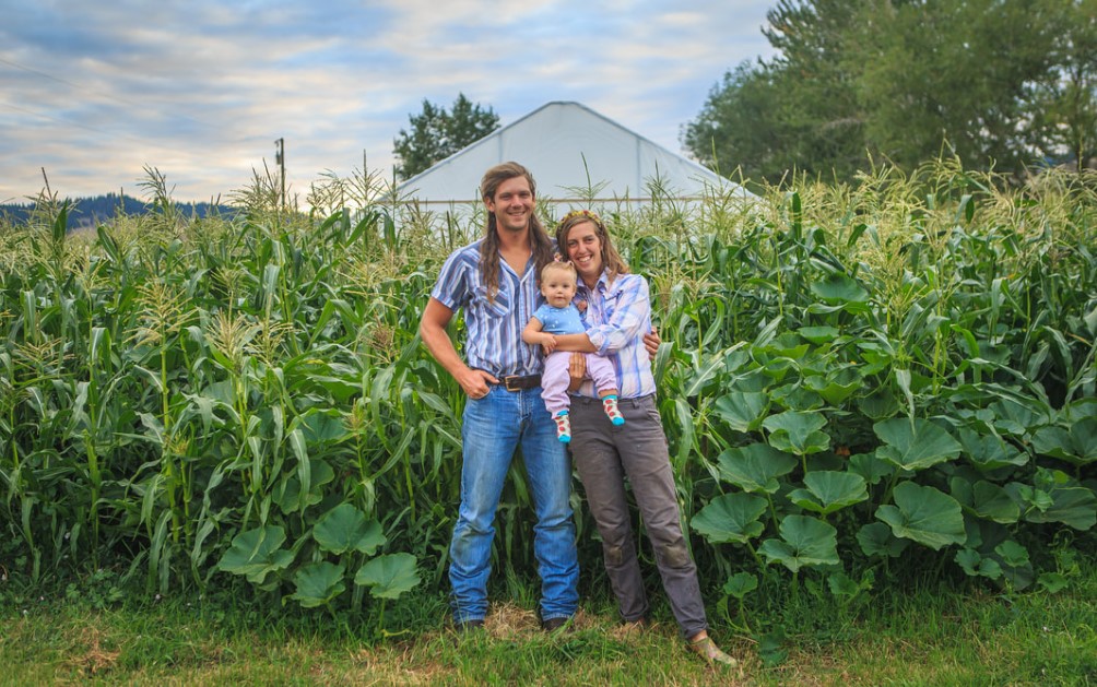 family of three poses in front of corn crop on a farm