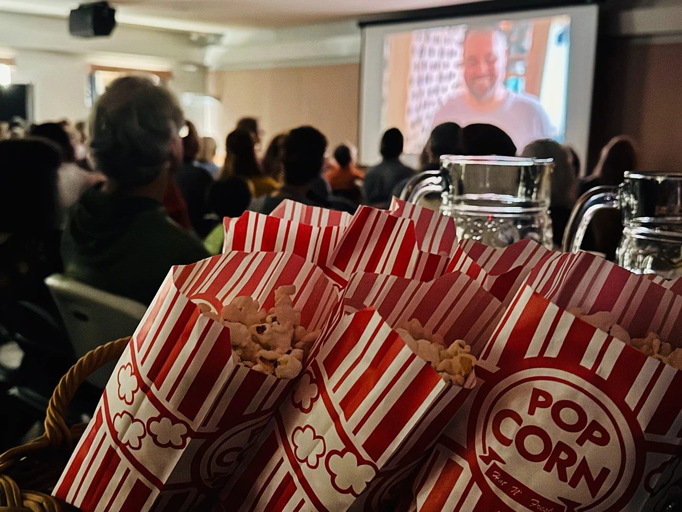bags of popcorn in the foreground with guests watching a film in the background
