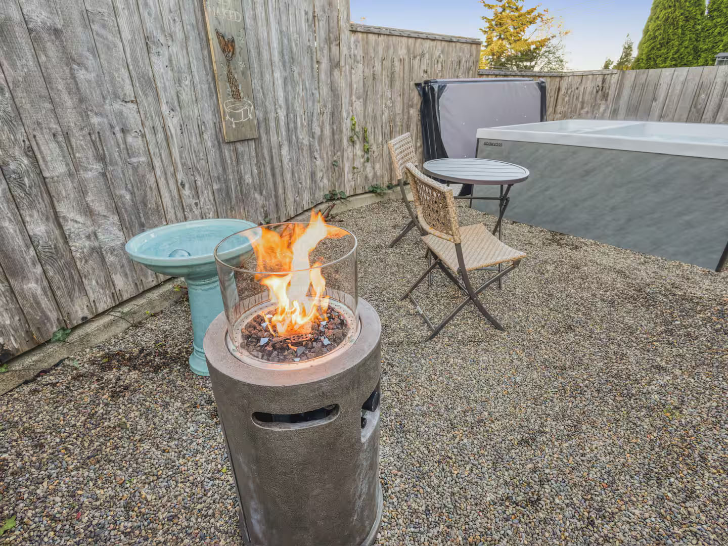 gravel patio with firepit, table and chairs and hot tub
