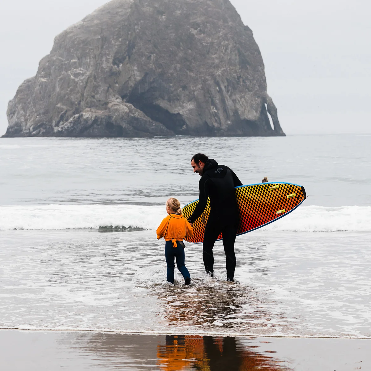 Father and daughter standing in shallow ocean water with surf board at Cape Kiwanda Longboard Classic