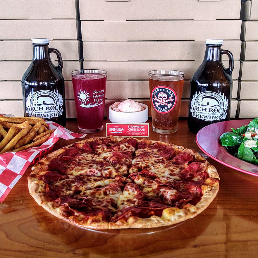 table with whole pizza, basket of french fries, salad, 2 full pint glasses, 2 growlers and a bowl of ice cream