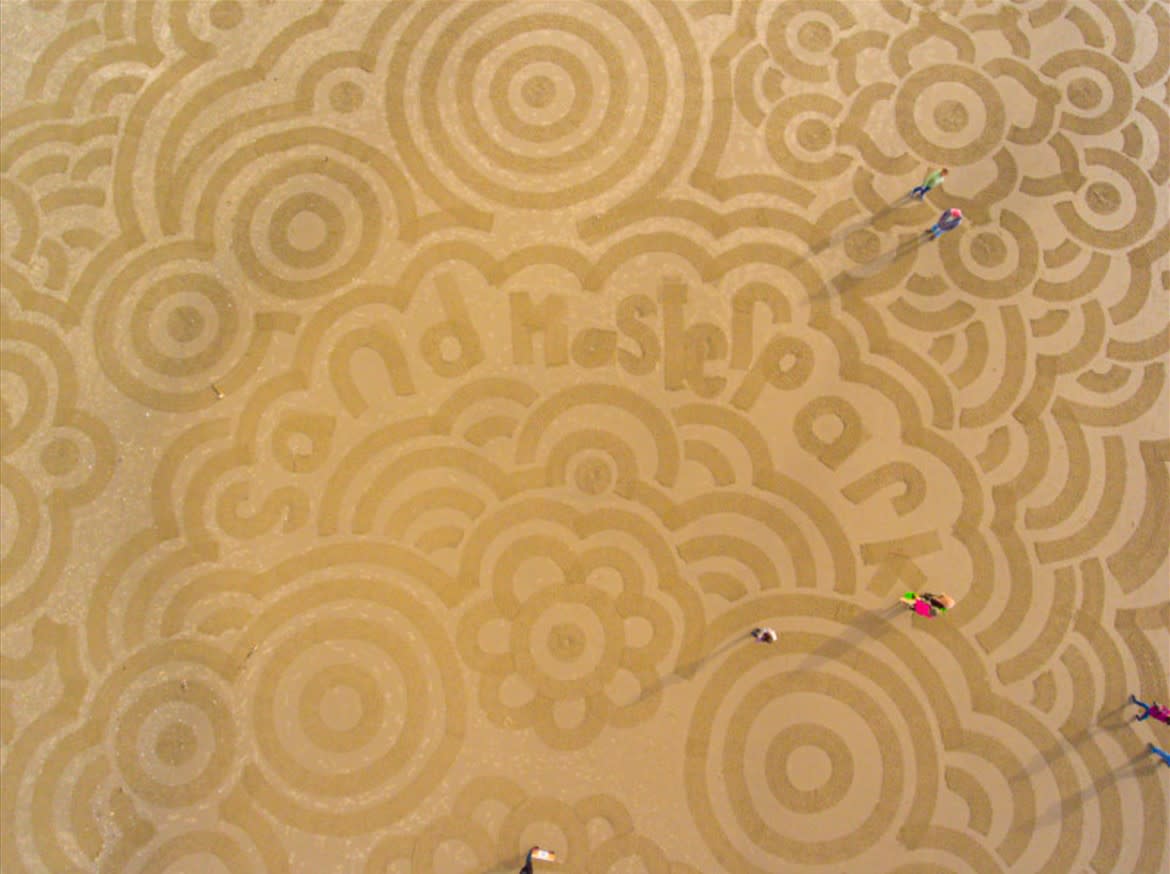 Aerial view of people walking over circular sand art on the beach