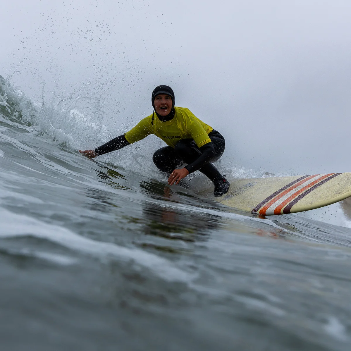 closeup of surfer riding wave and touching it as they pass by at Cape Kiwanda Longboard Classic