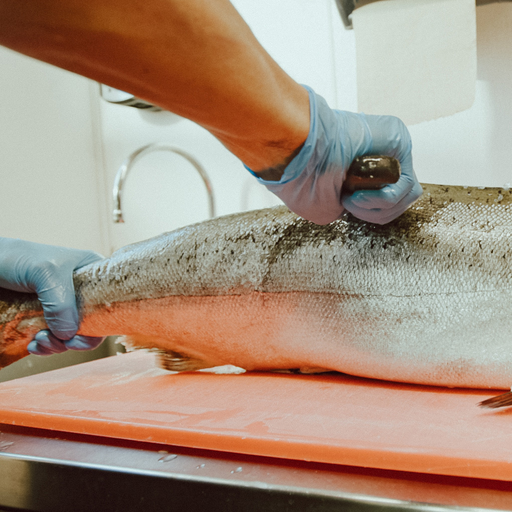 Ecola Seafoods cooks filleting salmon on cutting board in kitchen