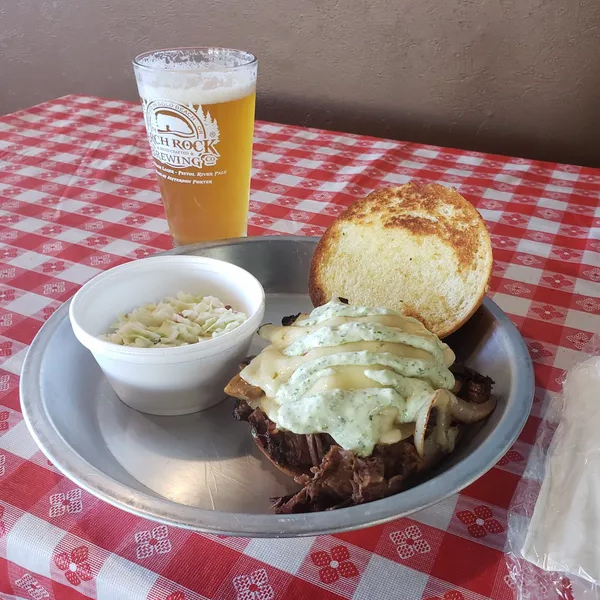 BBQ sandwich and coleslaw on a plate with a pint of beer next to it on a table with checkered tablecloth