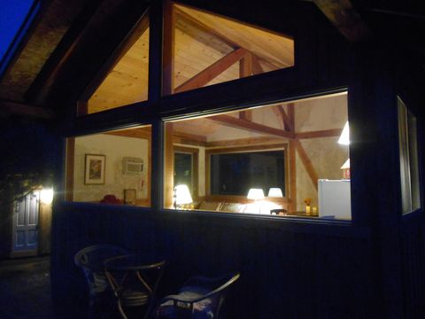 exterior of small cabin at night with large windows lights on inside