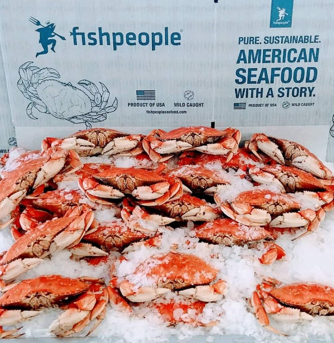 Fishpeople box and logo sit behind a huge pile of freshly caught dungeness crabs.