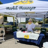 person stands behind table in farmers market booth