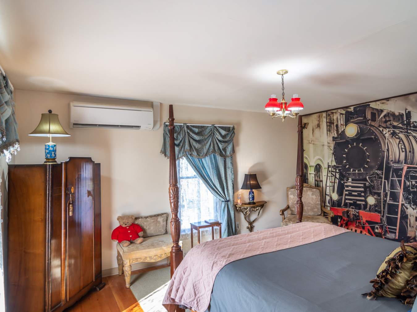 Train room with blue drapes, wall sized train print and tall wooden bedposts